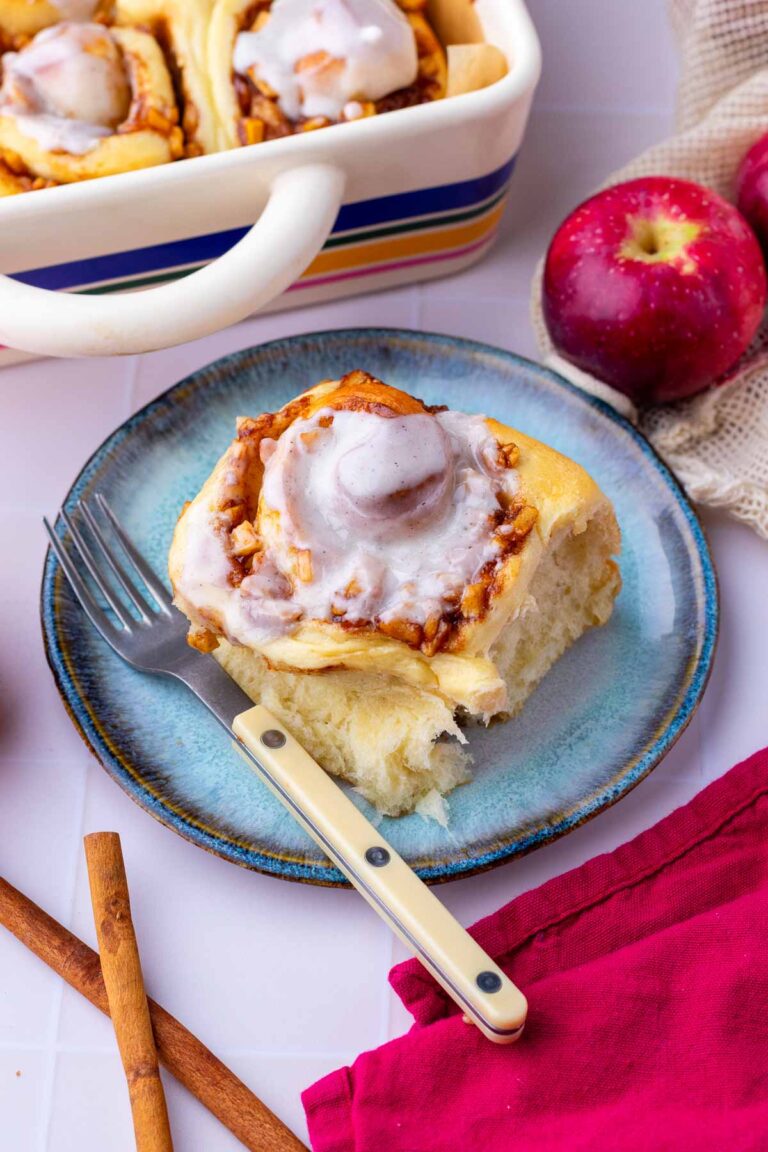sourdough apple cinnamon roll on a plate with a fork and apples in the background