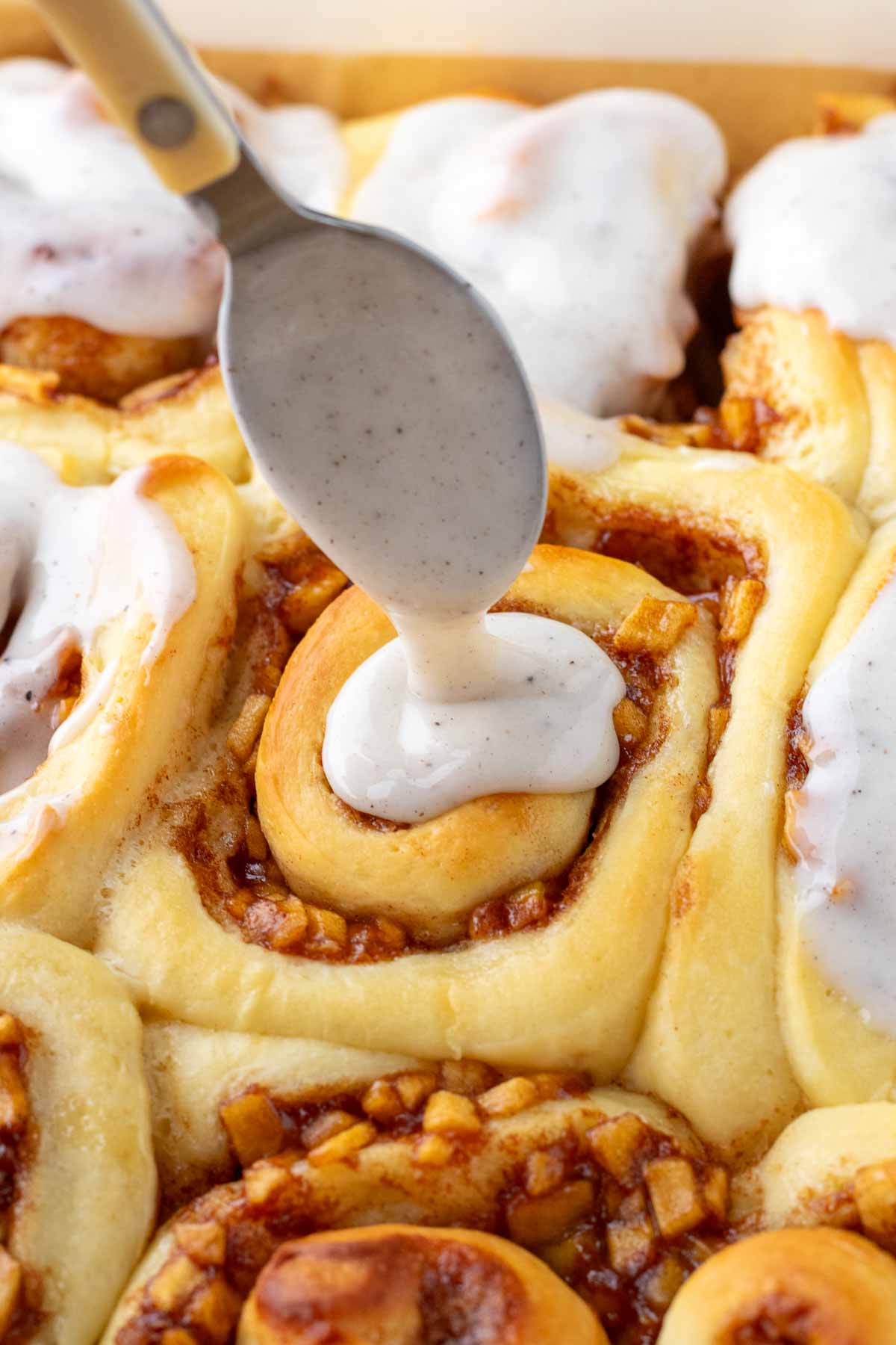 Spooning vanilla icing on sourdough apple cinnamon rolls
